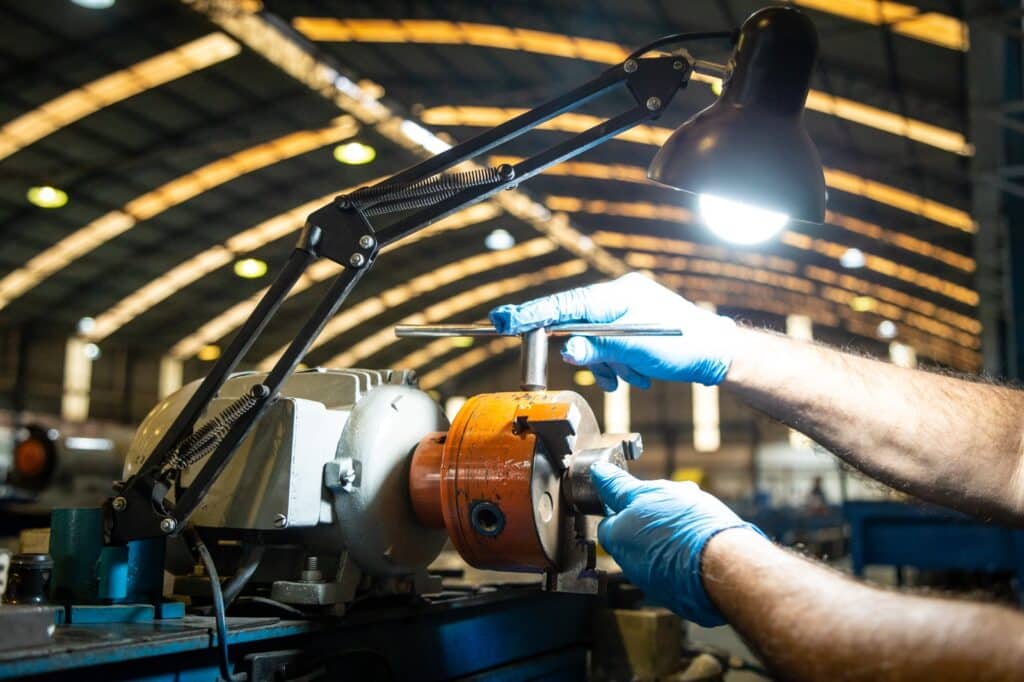 close-up de um equipamento industrial, uma máquina de conformação ou endireitamento de arames/tubos metálicos mostrando o processo de transformação sob demanda de aço inox.