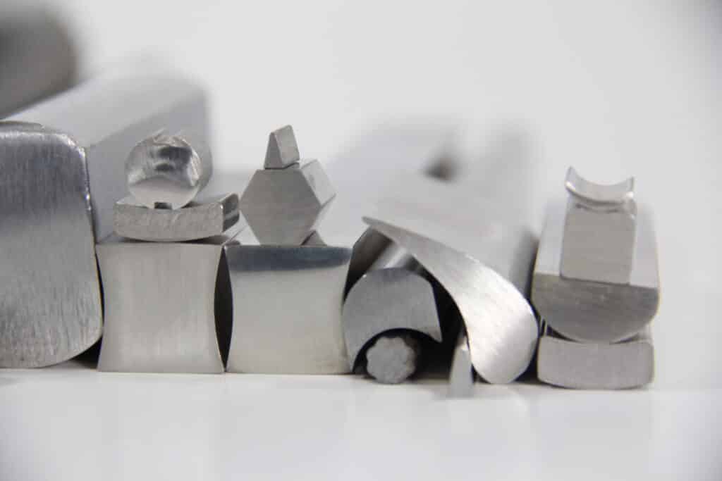 Diversos perfis metálicos de aço inoxidável com diferentes geometrias e seções transversais organizados